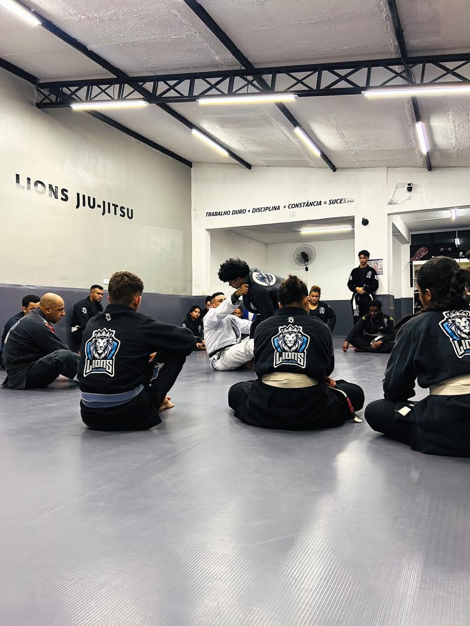 Alunos sentados no tatame durante a aula